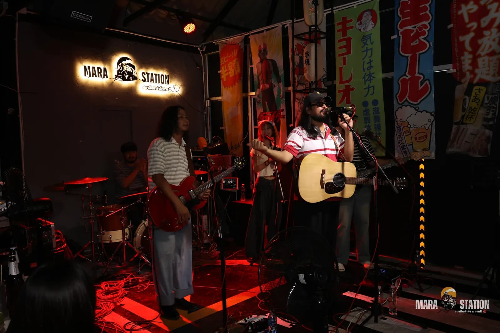 วงดนตรีสดเต็มวงบนเวที Mara Station ใต้แบนเนอร์เบียร์ญี่ปุ่น