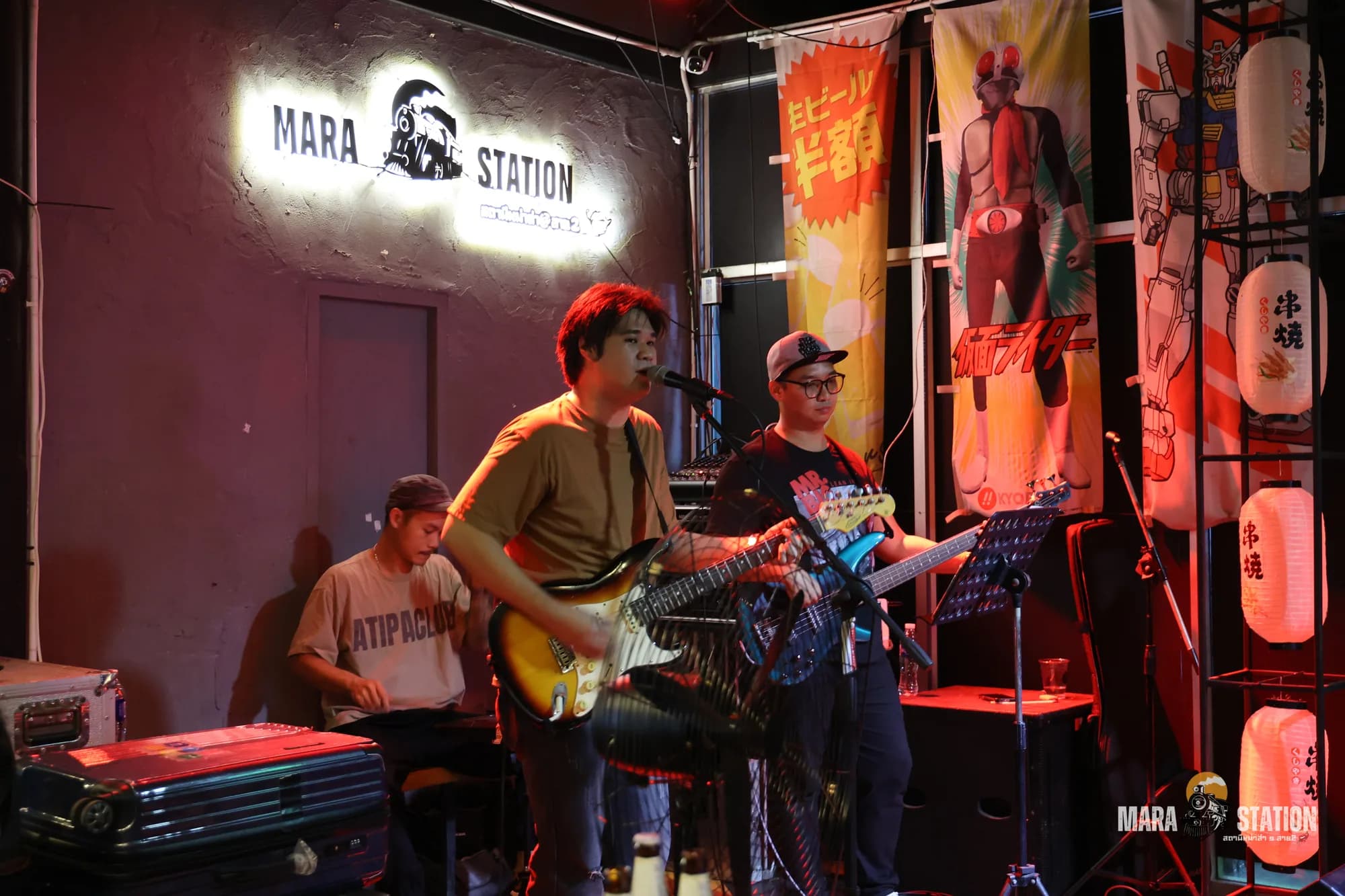 วงดนตรีสดเล่นเต็มวงใต้ป้ายไฟ Mara Station ท่ามกลางโคมไฟญี่ปุ่นและแบนเนอร์ izakaya